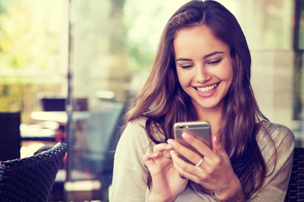 femme_alertes femme qui sourit en tenant son smartphone entre ses mains