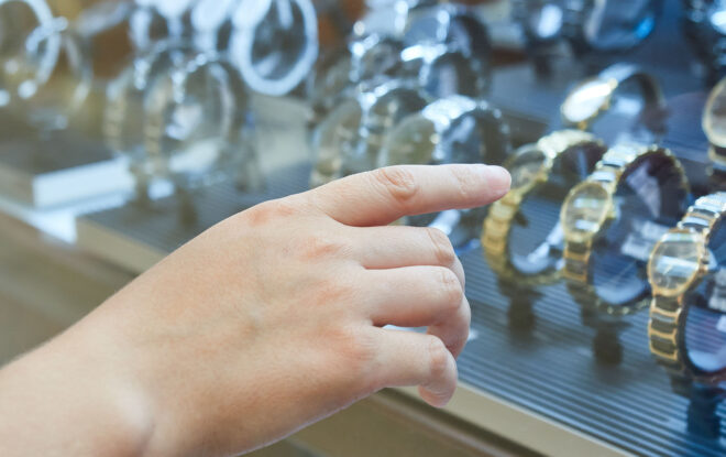 Mano che indica una vetrina di orologi di lusso in oro e acciaio inossidabile